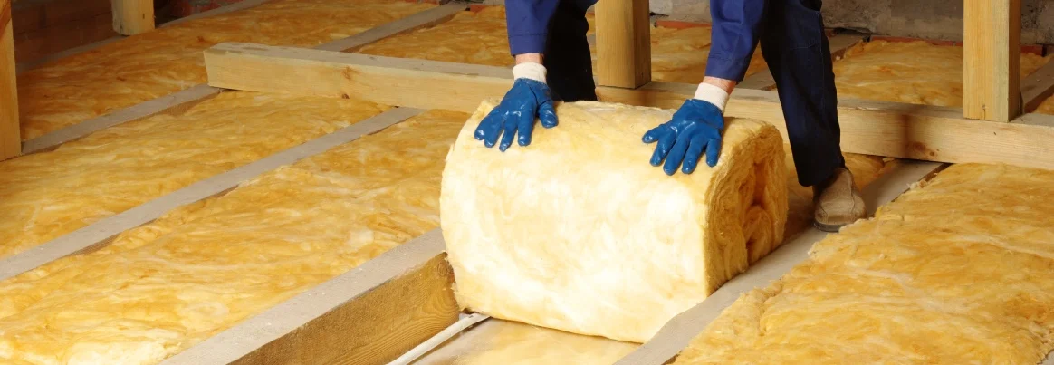 Eine Person dämmt eine Geschossdecke mit Dämmwolle.